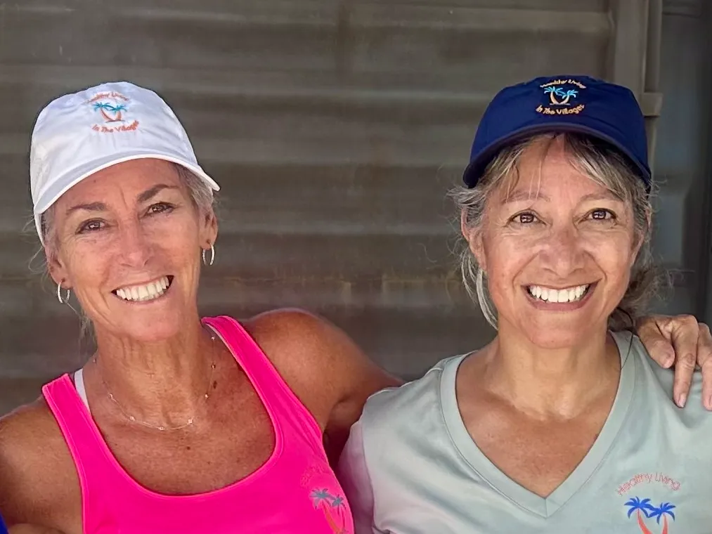 Two Villages Healthy Living hats, one white and one navy, both embroidered with the palm tree logo